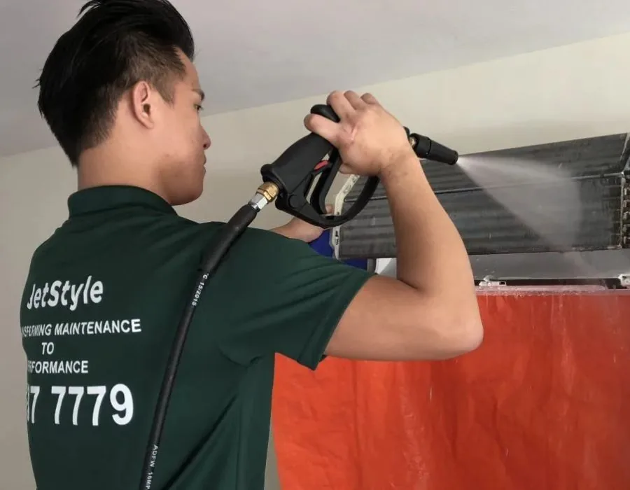 Jetstyle technician spraying cleaner on an air conditioning unit during maintenance