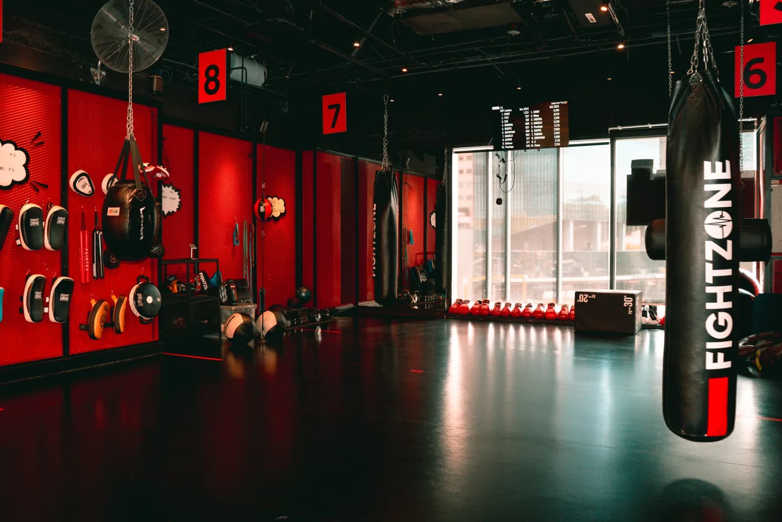 Boxing gym interior with red walls, hanging heavy bags, weight equipment, and floor-to-ceiling windows