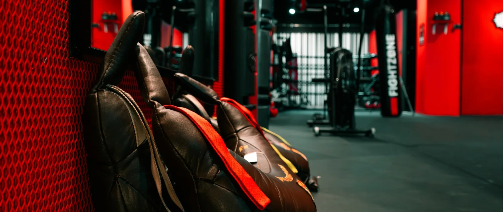 Boxing bags and training equipment in a modern gym with red walls and dark flooring