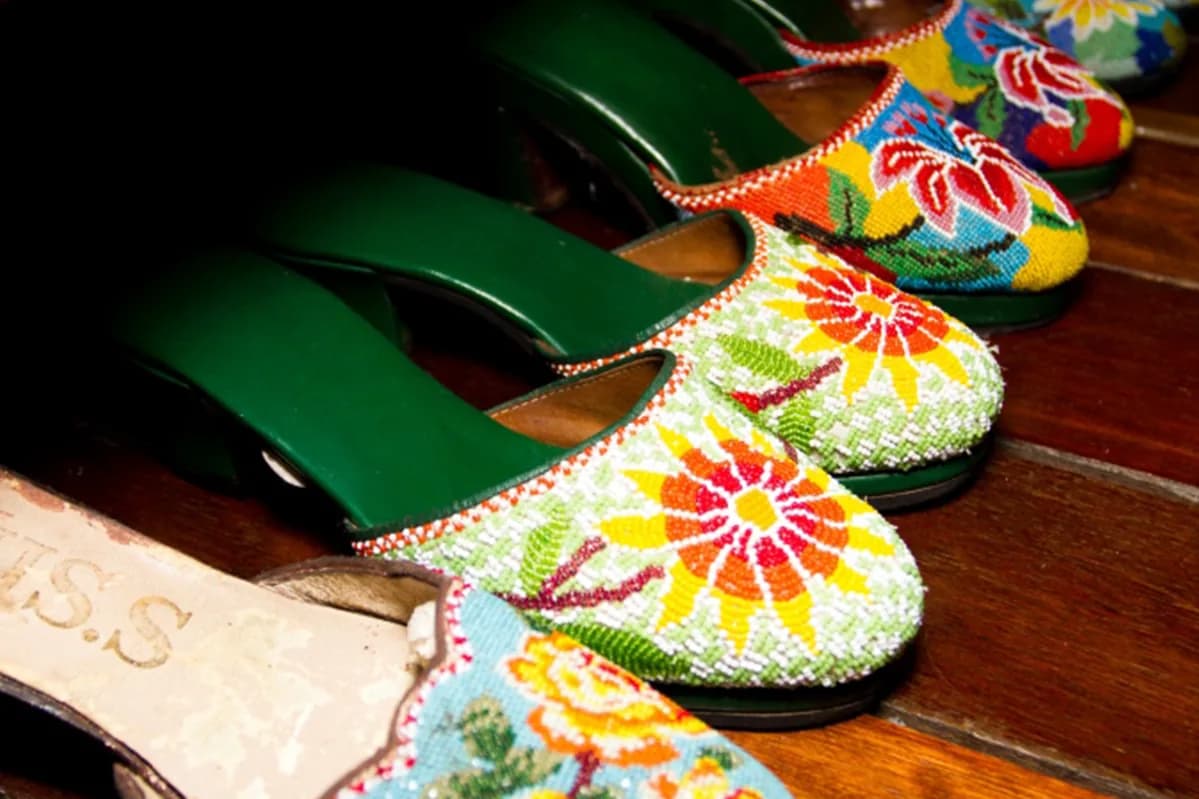 Row of colorful embroidered traditional slippers with beaded floral designs on wooden surface