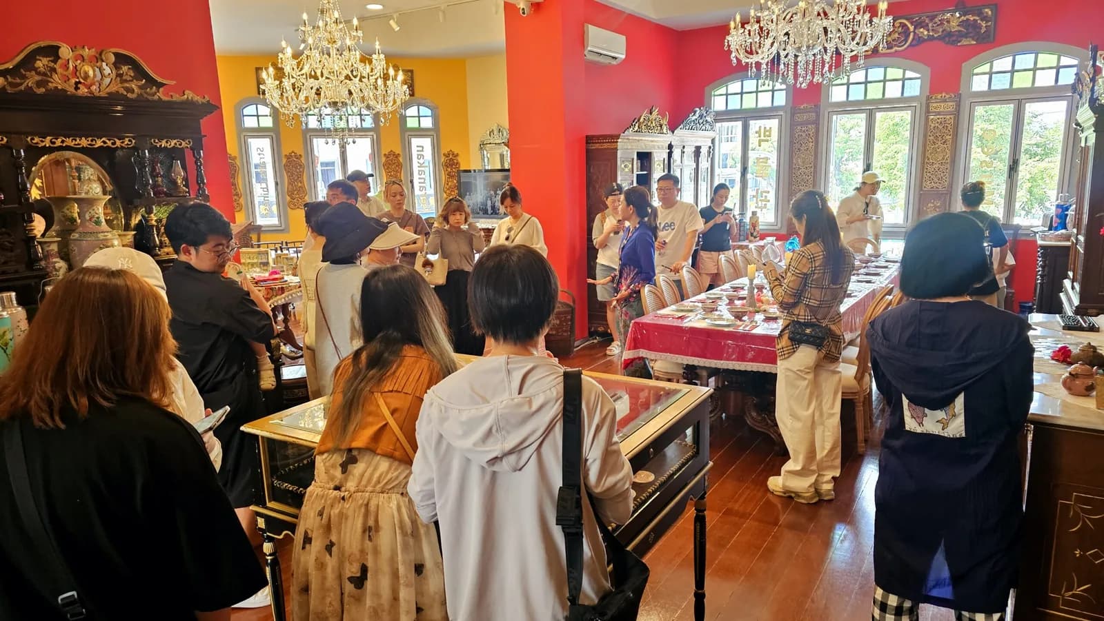 Visitors touring colorful interior of Peranakan mansion museum with ornate chandeliers and traditional furnishings