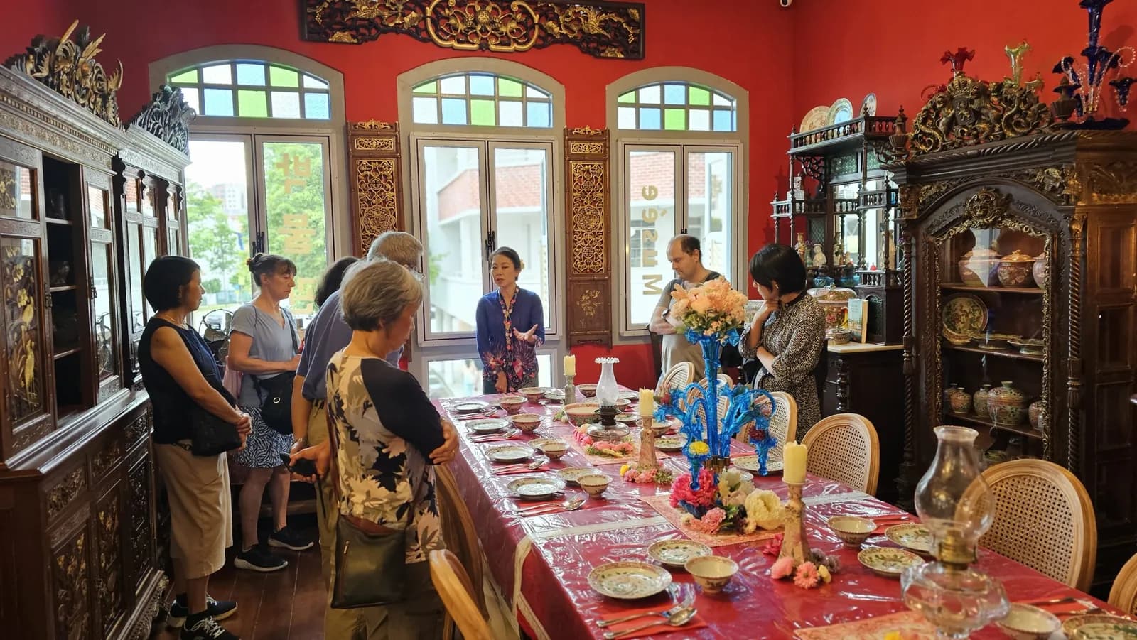 Ornate dining room with red walls and golden furnishings; visitors gathered around a set table