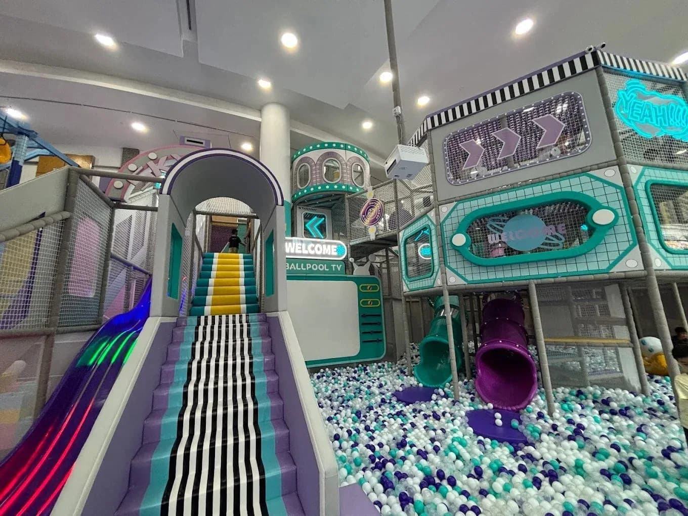 Colorful indoor play area with ball pool, neon-lit slides, and climbing structures
