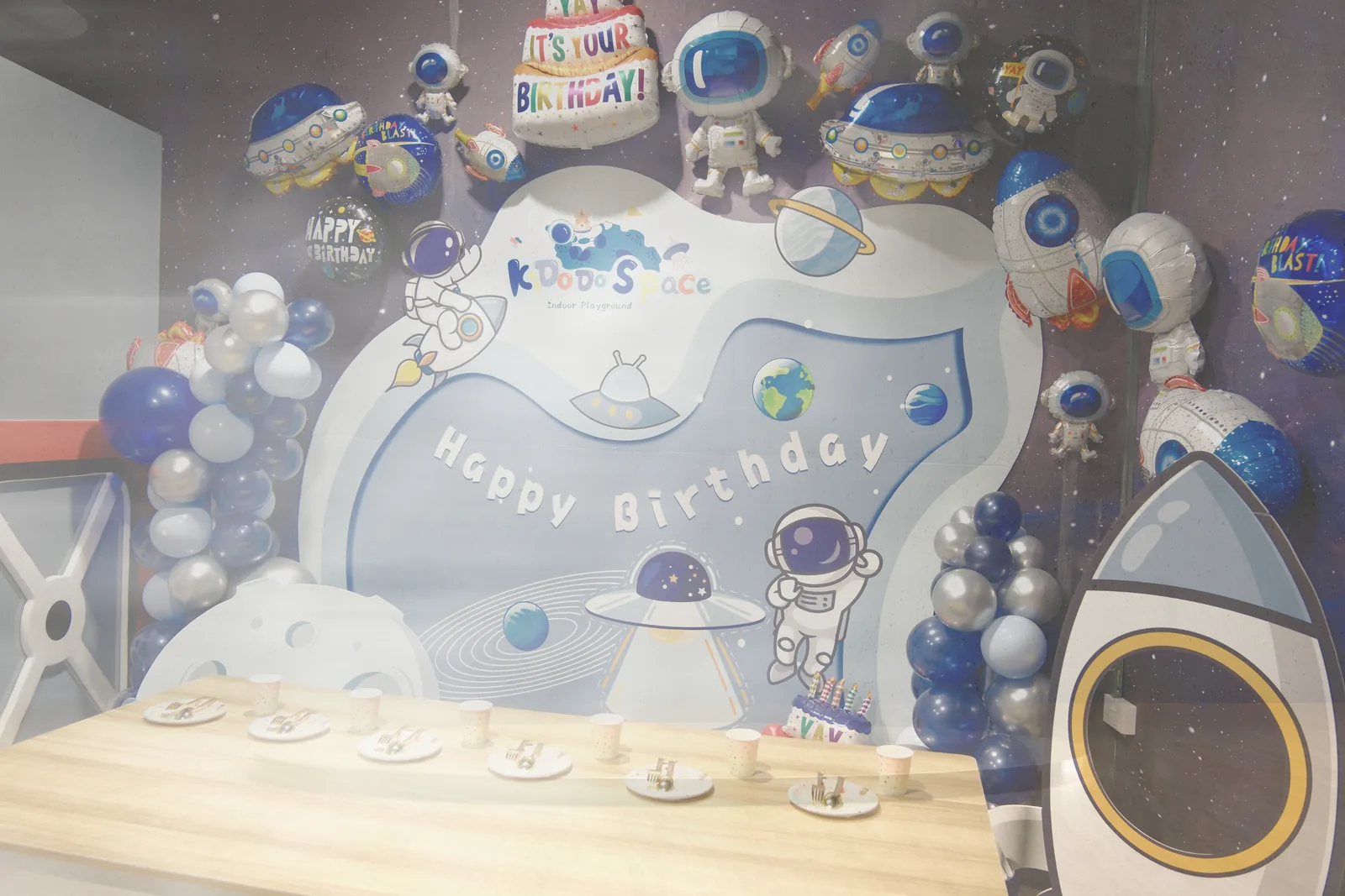Space-themed birthday party setup with astronaut decorations, balloons, and rocket props