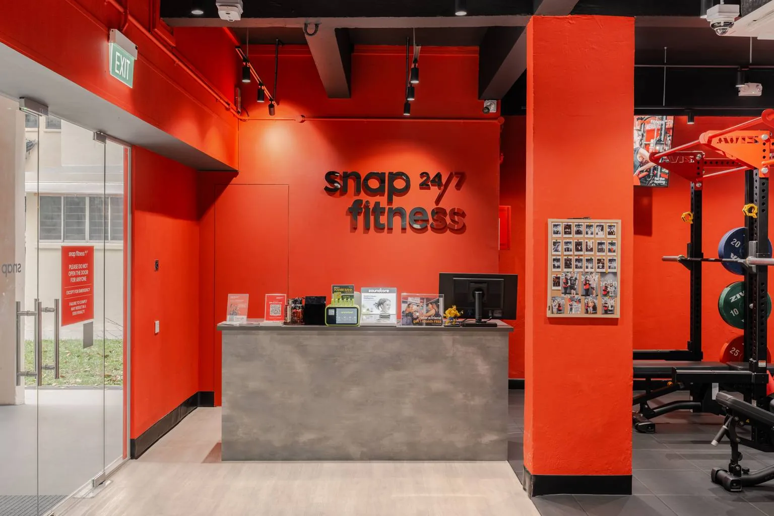 Snap Fitness gym entrance with red walls, gray reception desk, and fitness equipment visible