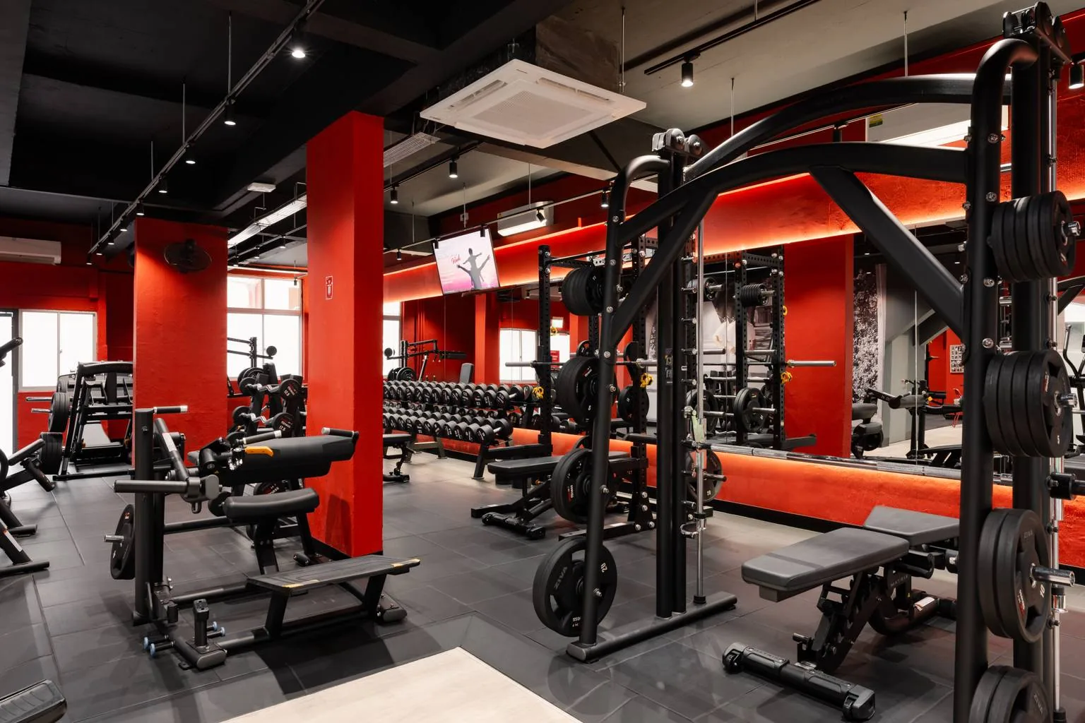 Bright gym interior with red walls, weight racks, barbells, and cardio equipment