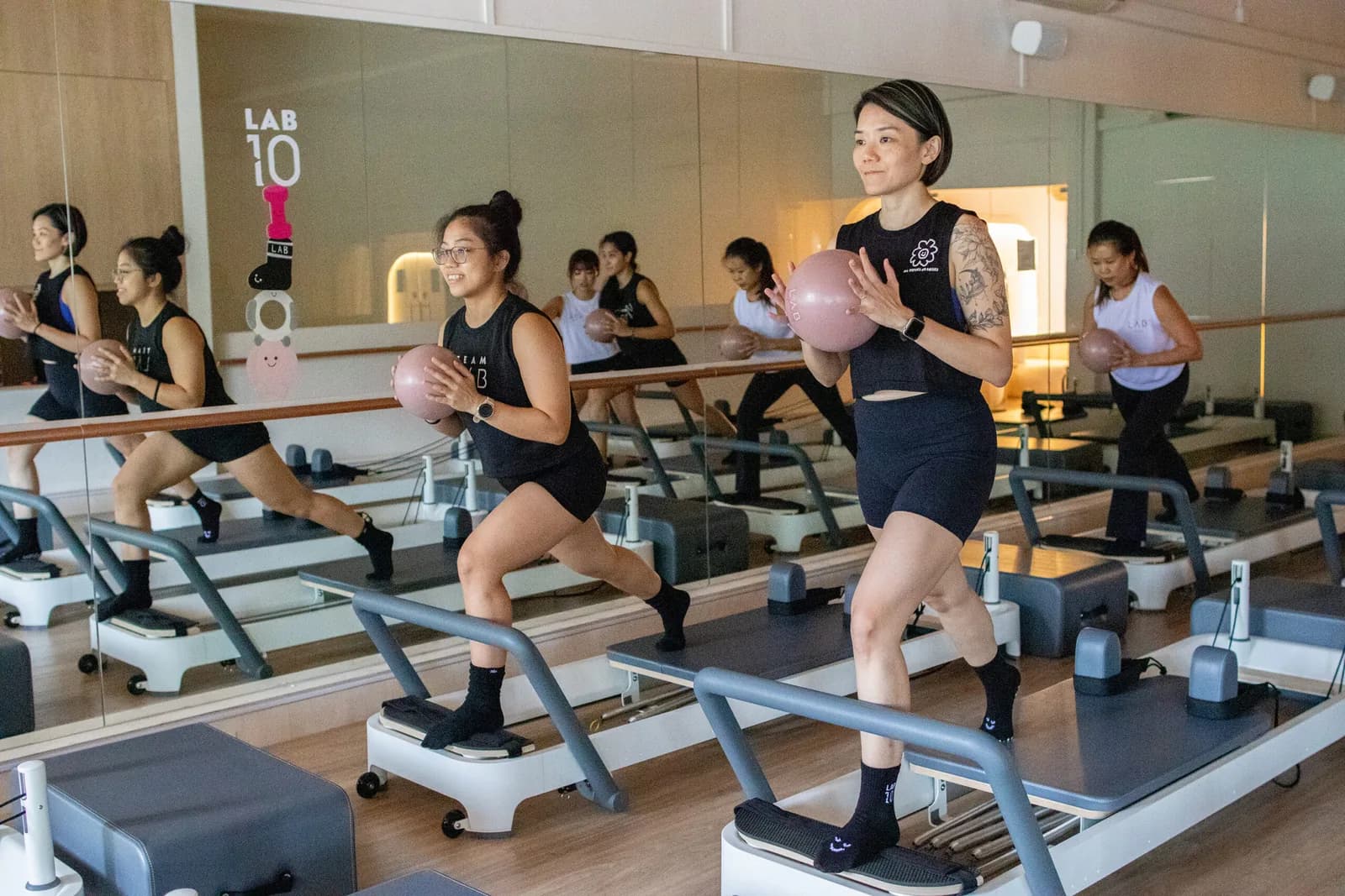 Group reformer pilates class with participants on machines holding pink balls