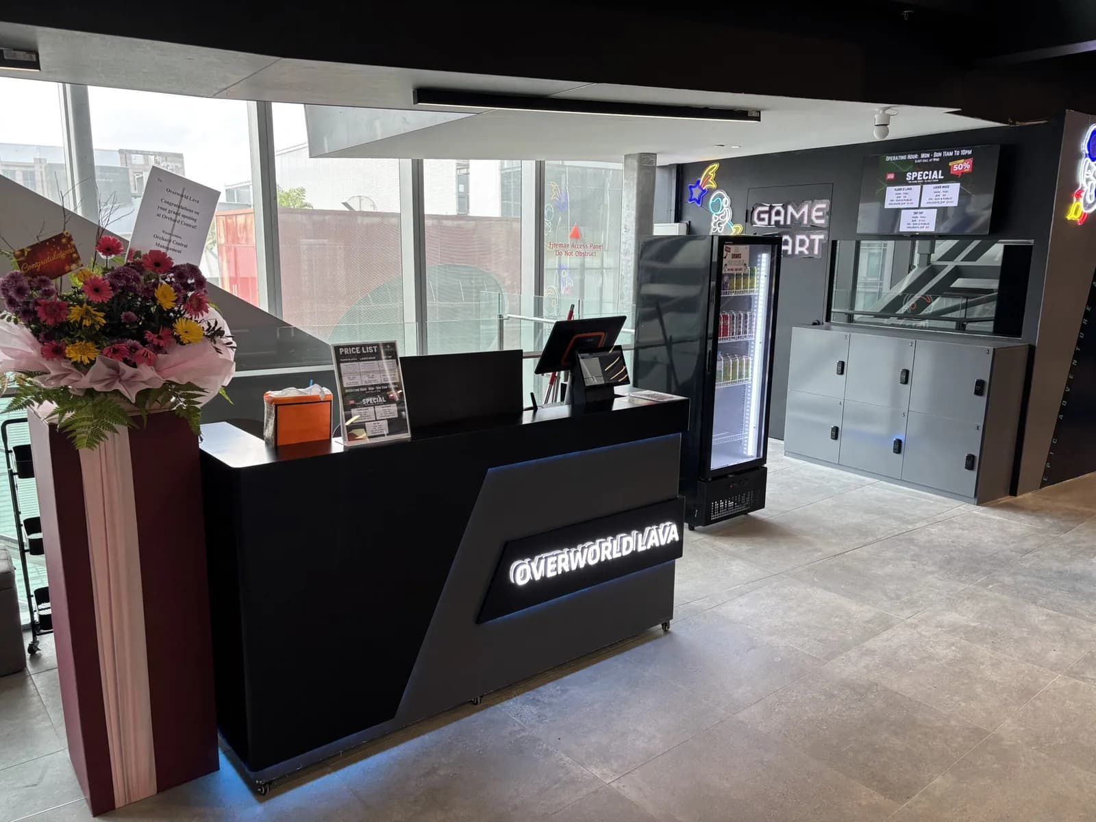 Modern gaming venue reception area with black counter, flower arrangement, and entertainment screens