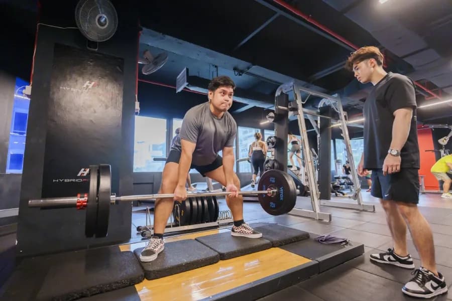 Trainer supervising client doing barbell deadlift in bright, modern gym with equipment