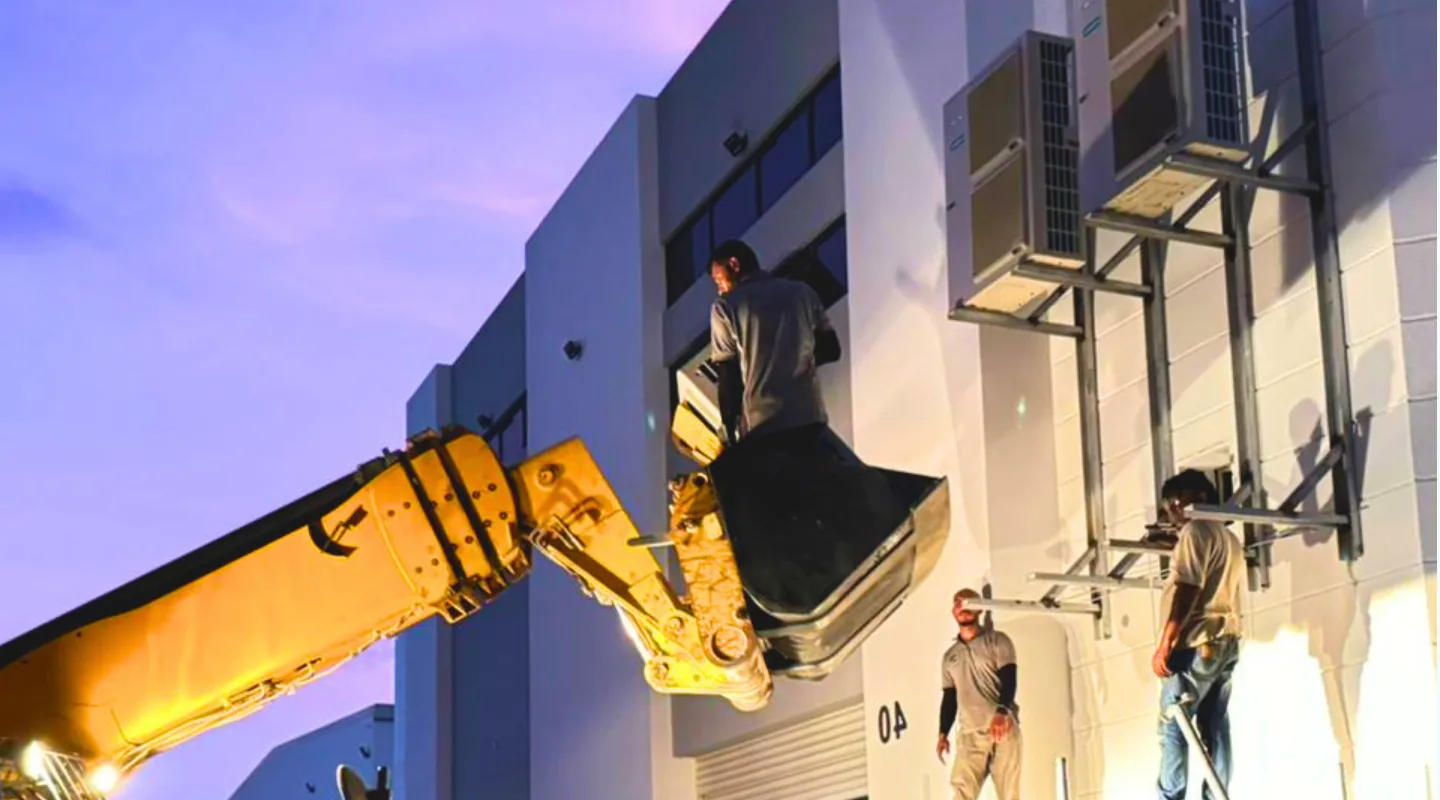 Technicians on lift platform working on AC unit mounted on building exterior