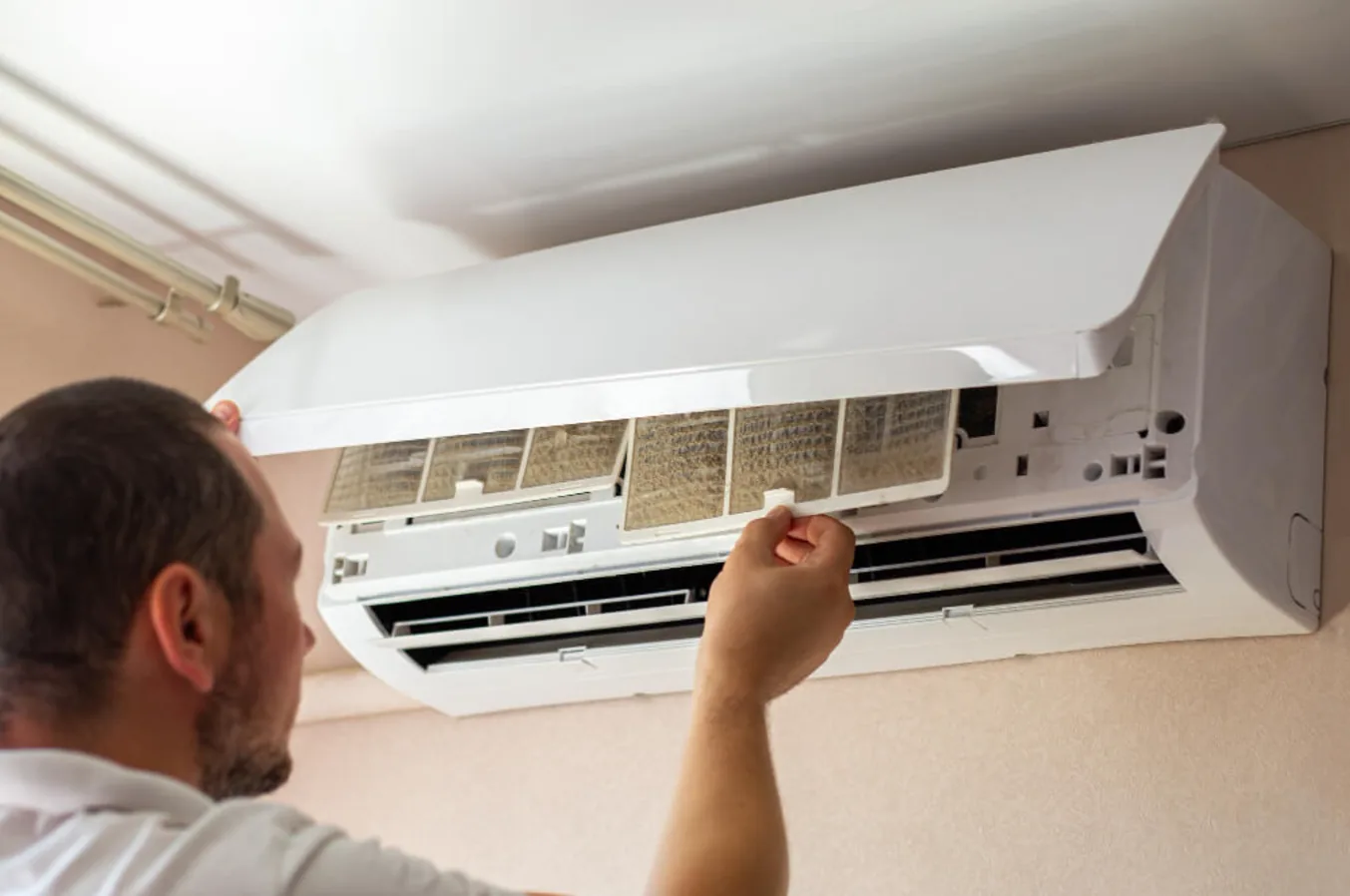 Technician removing filter from wall-mounted air conditioner during servicing
