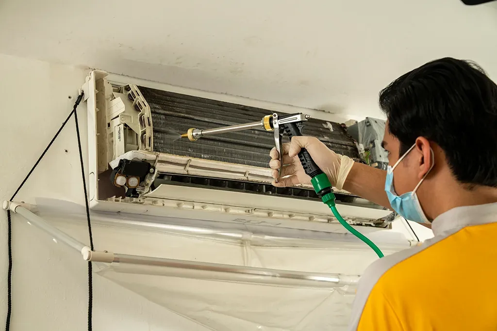 Technician servicing an air conditioner unit, cleaning internal parts with tools