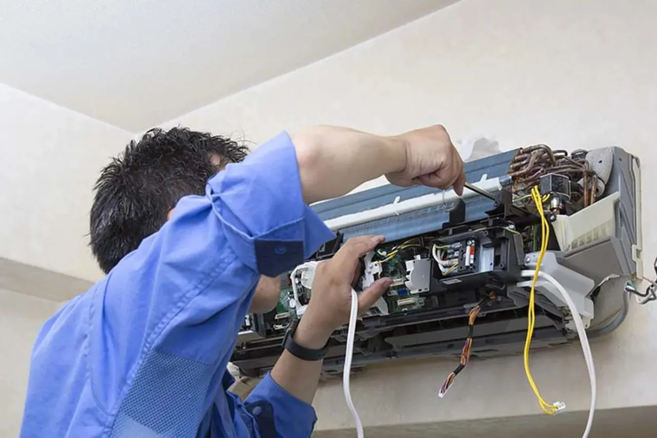 Technician servicing AC unit internals with exposed circuits and wires