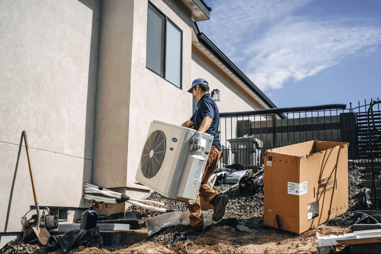Technician carrying AC condenser unit during installation at building exterior