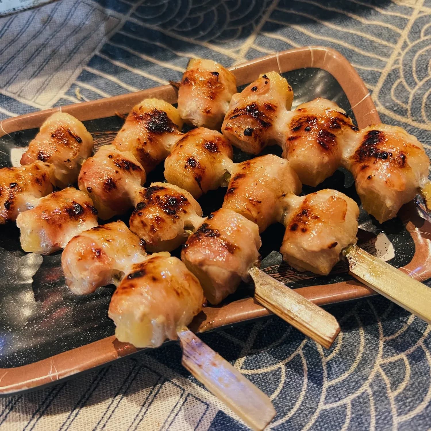 Golden-brown grilled chicken skewers with char marks on a black plate with wooden handles