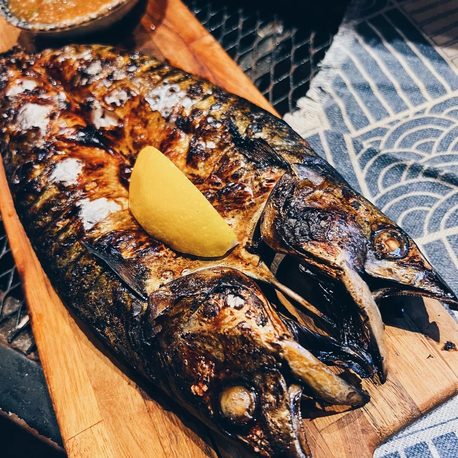 Grilled whole fish with lemon wedge on wooden serving board