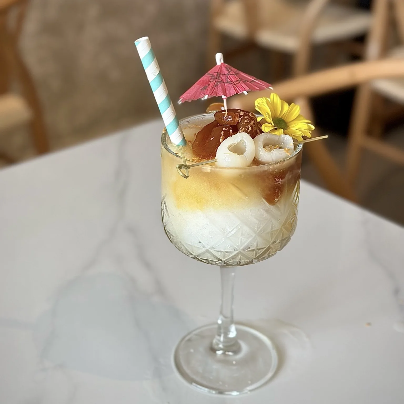 Tropical cocktail with yellow and white layers, umbrella and flower garnish in textured glass
