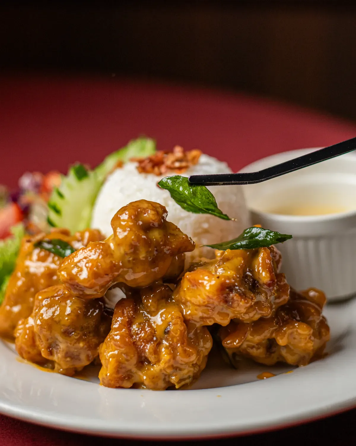 Glazed chicken pieces with basil garnish and white dipping sauce on a plate