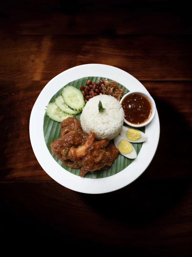 Plate of braised meat with white rice, cucumber, egg, and gravy served on banana leaf