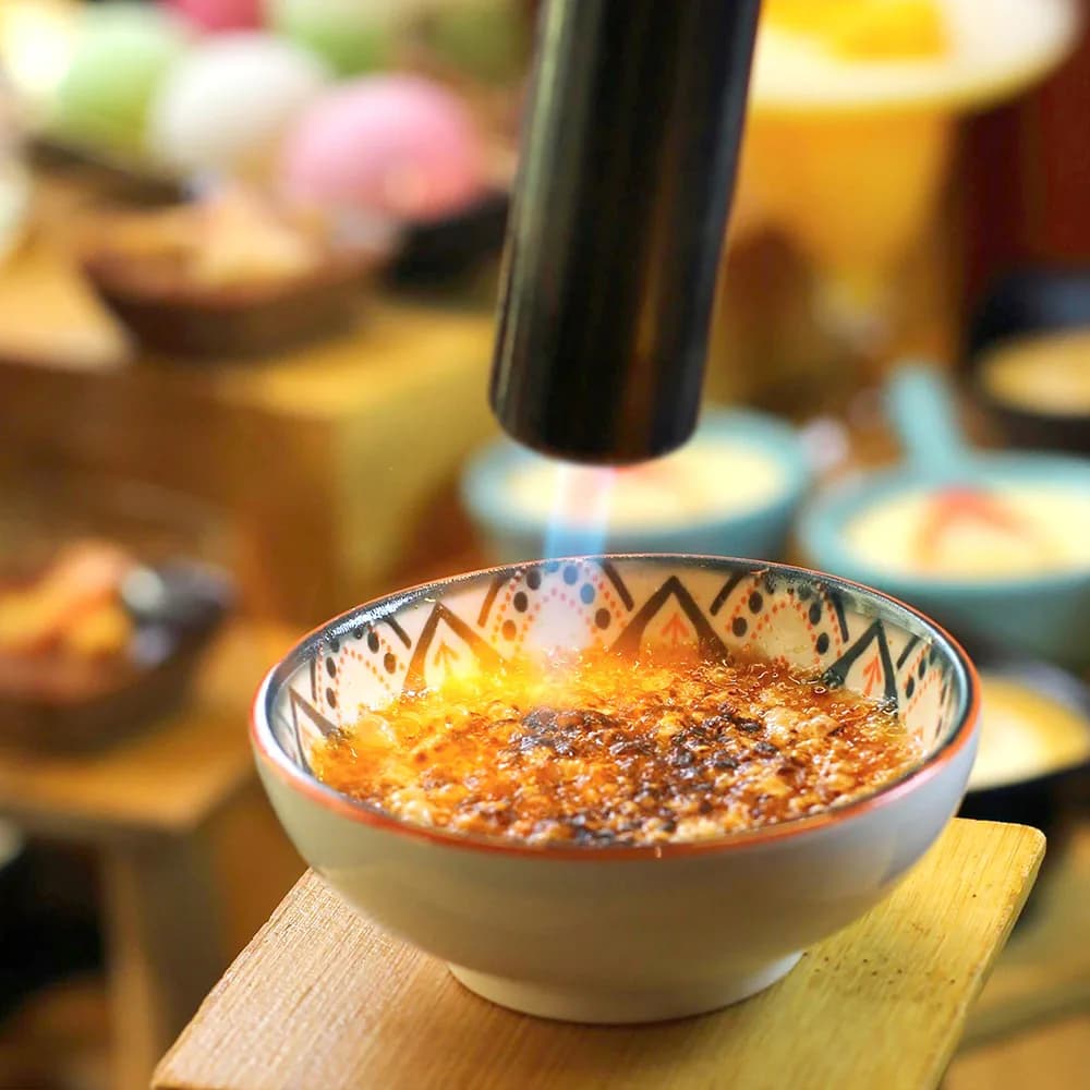 Golden soup in a patterned ceramic bowl with a ladle, surrounded by other dishes at a restaurant table.