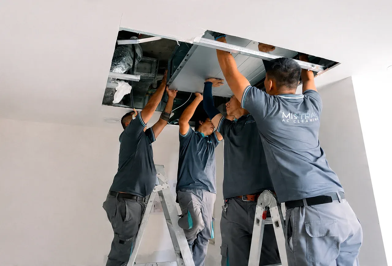Four AC technicians in Mistral uniforms installing or servicing an overhead air conditioning unit together