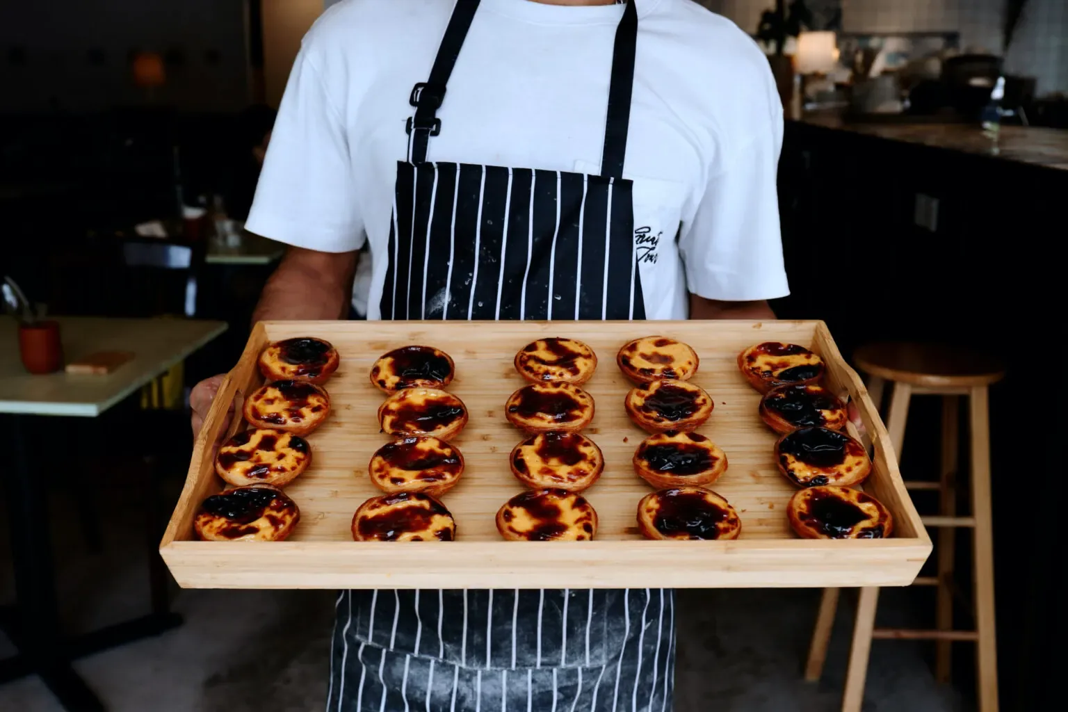 Chef holding wooden tray of caramelized Portuguese custard tarts in restaurant kitchen