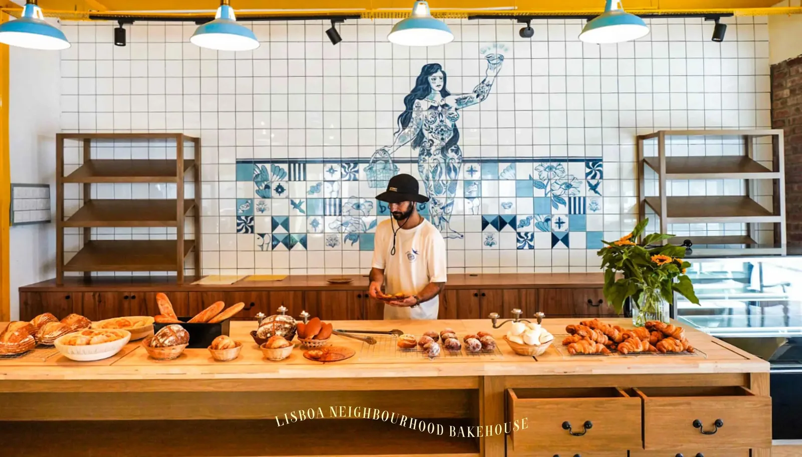 Baker behind counter with fresh baked goods in modern bakery with blue and white tile wall