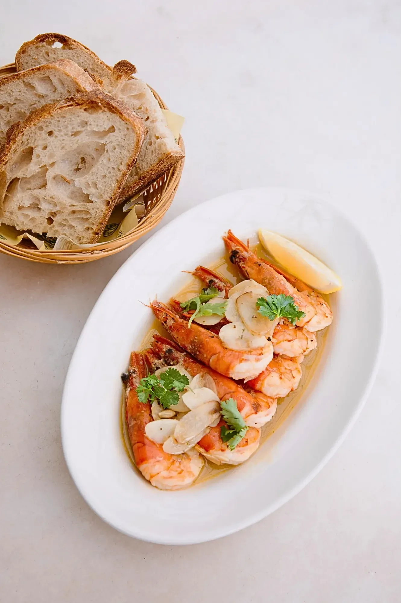Garlic butter prawns with almonds and cilantro on white plate, toasted bread in basket