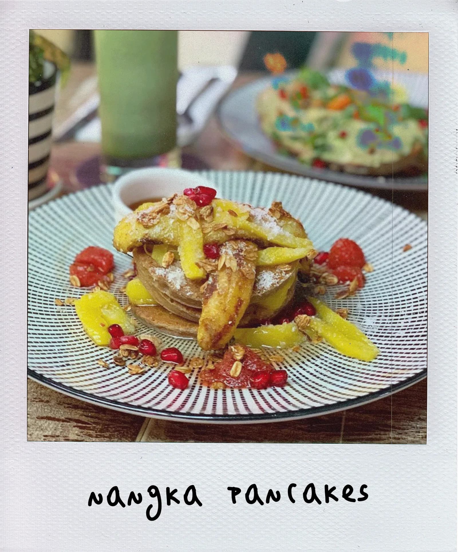 Mango pancakes stack with fresh mango slices, pomegranate seeds, and granola on patterned white plate