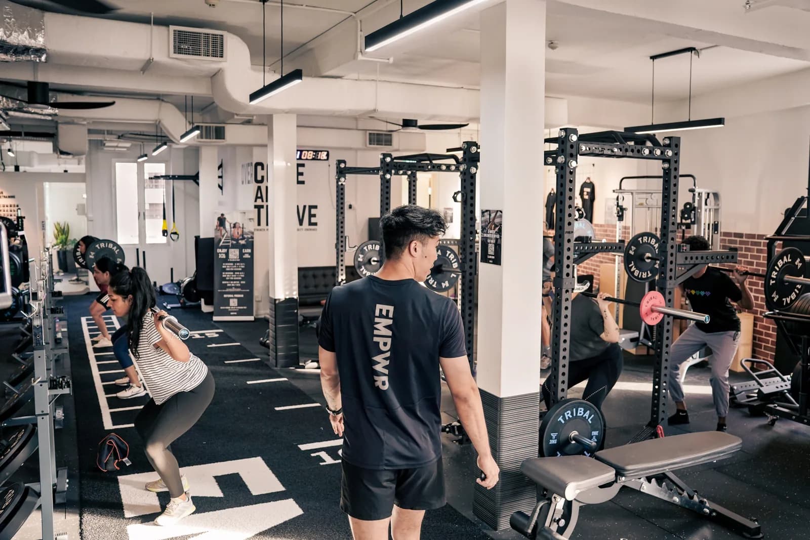 Gym interior with clients using squat racks and training equipment in a bright, spacious facility.